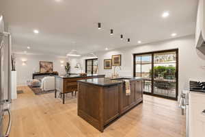 Kitchen featuring sink, high end refrigerator, light hardwood / wood-style flooring, dark stone countertops, and a kitchen island with sink