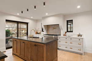 Kitchen with sink, light hardwood / wood-style floors, white cabinets, a center island with sink, and decorative backsplash