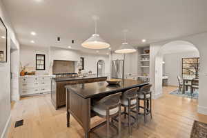 Kitchen with high quality fridge, a breakfast bar area, white cabinets, hanging light fixtures, and a kitchen island with sink