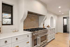 Kitchen featuring white cabinetry, light wood-type flooring, double oven range, custom range hood, and decorative backsplash