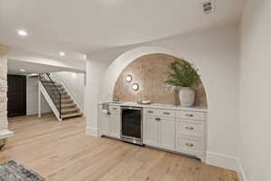 Bar featuring wine cooler, backsplash, white cabinetry, and light hardwood / wood-style floors