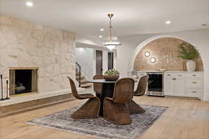 Dining room with wine cooler, a stone fireplace, light hardwood / wood-style flooring, and indoor bar