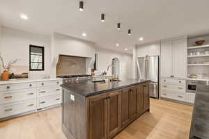 Kitchen featuring sink, high end refrigerator, light wood-type flooring, a kitchen island with sink, and white cabinets