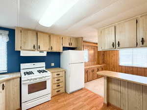 Kitchen featuring a textured ceiling, light brown cabinets, light wood-type flooring, wooden walls, and white appliances