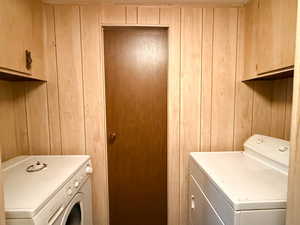 Laundry room with cabinets, washer and dryer, and wood walls