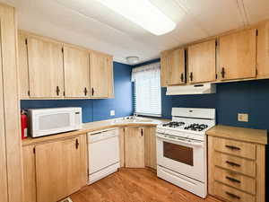 Kitchen with white appliances, light brown cabinetry, sink, and light hardwood / wood-style flooring