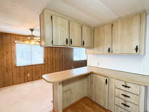 Kitchen featuring light brown cabinets, kitchen peninsula, ceiling fan, and wood walls