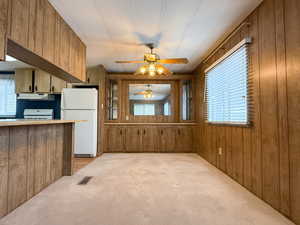 Kitchen with light colored carpet, plenty of natural light, wooden walls, and white fridge