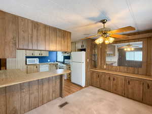 Kitchen with sink, white appliances, light colored carpet, kitchen peninsula, and wood walls