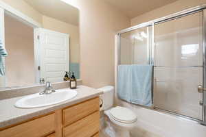 Full bathroom with vanity, tile patterned floors, shower / bath combination with glass door, and toilet