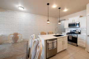 Kitchen featuring appliances with stainless steel finishes, sink, a center island with sink, and white cabinets