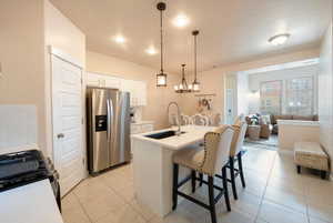 Kitchen featuring sink, white cabinetry, hanging light fixtures, stainless steel appliances, and an island with sink