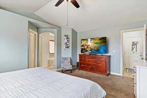 Bedroom featuring connected bathroom, vaulted ceiling, light colored carpet, and ceiling fan