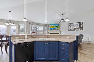 Kitchen with blue cabinets, black dishwasher, sink, hanging light fixtures, and a kitchen island with sink