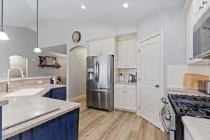 Kitchen with lofted ceiling, sink, hanging light fixtures, stainless steel appliances, and light hardwood / wood-style floors