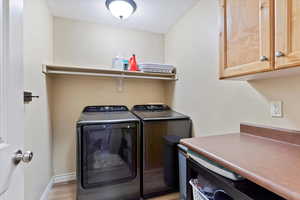 Clothes washing area with cabinets, light hardwood / wood-style flooring, and washing machine and clothes dryer