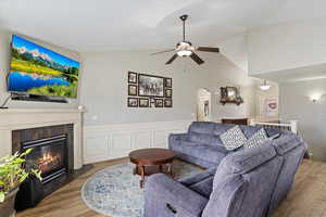 Living room featuring a tiled fireplace, vaulted ceiling, hardwood / wood-style flooring, and ceiling fan