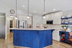 Kitchen featuring stainless steel appliances, a kitchen island with sink, pendant lighting, and white cabinets