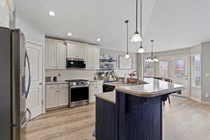 Kitchen featuring a breakfast bar area, a center island with sink, appliances with stainless steel finishes, pendant lighting, and light hardwood / wood-style floors