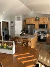 Kitchen featuring lofted ceiling, a breakfast bar, light hardwood / wood-style flooring, a kitchen island, and stainless steel appliances