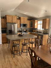 Kitchen with vaulted ceiling, a kitchen breakfast bar, a center island, light hardwood / wood-style floors, and stainless steel appliances