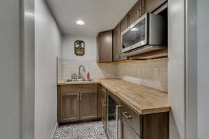 Kitchen featuring sink, wine cooler, wooden counters, backsplash, and a textured ceiling