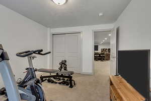 Exercise area with light colored carpet and a textured ceiling