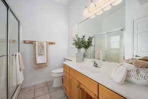 Bathroom with tile patterned floors, toilet, a chandelier, vanity, and a shower with door