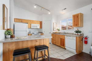 Kitchen with lofted ceiling, sink, a kitchen breakfast bar, kitchen peninsula, and white appliances