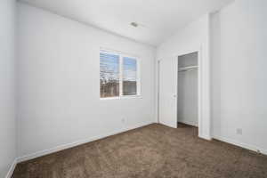 Unfurnished bedroom with lofted ceiling, dark carpet, and a closet