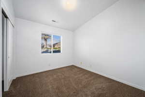 Unfurnished bedroom featuring lofted ceiling, a closet, and dark colored carpet