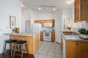 Kitchen featuring lofted ceiling, sink, a breakfast bar area, kitchen peninsula, and white appliances