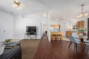 Living room with lofted ceiling, sink, ceiling fan with notable chandelier, and dark wood-type flooring