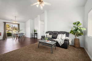 Living room with dark wood-type flooring, vaulted ceiling, and ceiling fan with notable chandelier