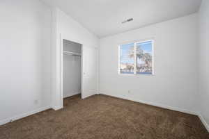 Unfurnished bedroom featuring dark carpet, vaulted ceiling, and a closet