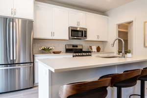 Kitchen with white cabinetry, sink, a kitchen breakfast bar, decorative backsplash, and stainless steel appliances