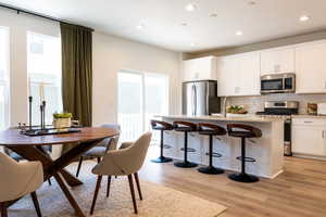 Kitchen with white cabinetry, appliances with stainless steel finishes, a kitchen island with sink, and a healthy amount of sunlight