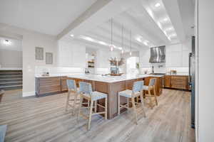 Kitchen featuring a spacious island, wall chimney range hood, hanging light fixtures, and white cabinets