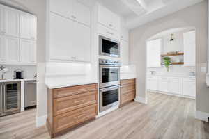 Kitchen with white cabinetry, wine cooler, light hardwood / wood-style flooring, and appliances with stainless steel finishes