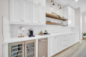 Bar with wine cooler, backsplash, white cabinetry, and light wood-type flooring