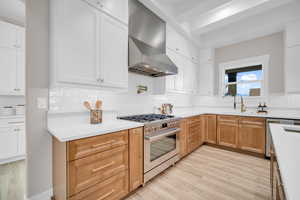 Kitchen featuring white cabinetry, stainless steel range with gas stovetop, range hood, and sink