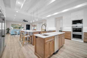 Kitchen featuring appliances with stainless steel finishes, pendant lighting, sink, white cabinets, and a center island with sink