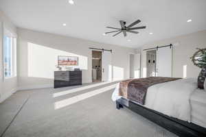 Bedroom with ceiling fan, light colored carpet, and a barn door