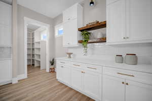 Bar with decorative backsplash, white cabinets, and light hardwood / wood-style flooring