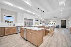 Kitchen with appliances with stainless steel finishes, an island with sink, sink, white cabinets, and beam ceiling