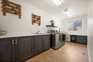 Laundry room with independent washer and dryer, cabinets, light tile patterned flooring, and sink