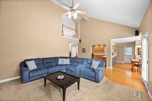 Carpeted living room featuring ceiling fan and high vaulted ceiling