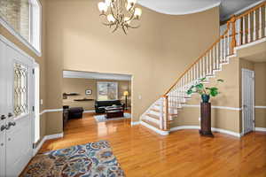 Foyer entrance with a notable chandelier, crown molding, wood-type flooring, and a high ceiling