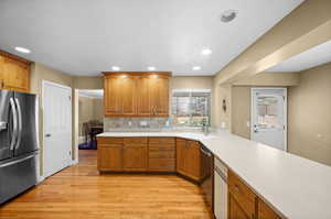 Kitchen with sink, stainless steel appliances, light hardwood / wood-style floors, decorative backsplash, and kitchen peninsula