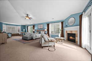 Carpeted bedroom featuring lofted ceiling, a tiled fireplace, and ceiling fan